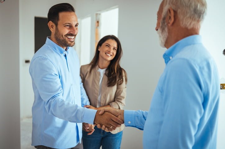 Happy couple buying a new home and handshaking with their real estate agent.